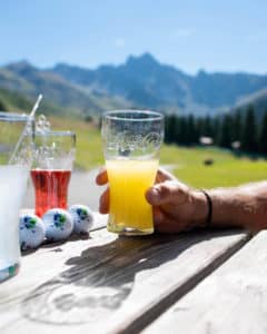 Golf Club de Courchevel | ©@roman.fln , verre de jus d'orange et balles de golf avec vue sur montagne