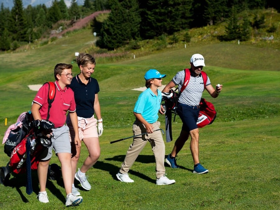 Couple et deux enfants joueurs de golf marchant sur le fairway du trou n°5 du Golf Club de Courchevel.