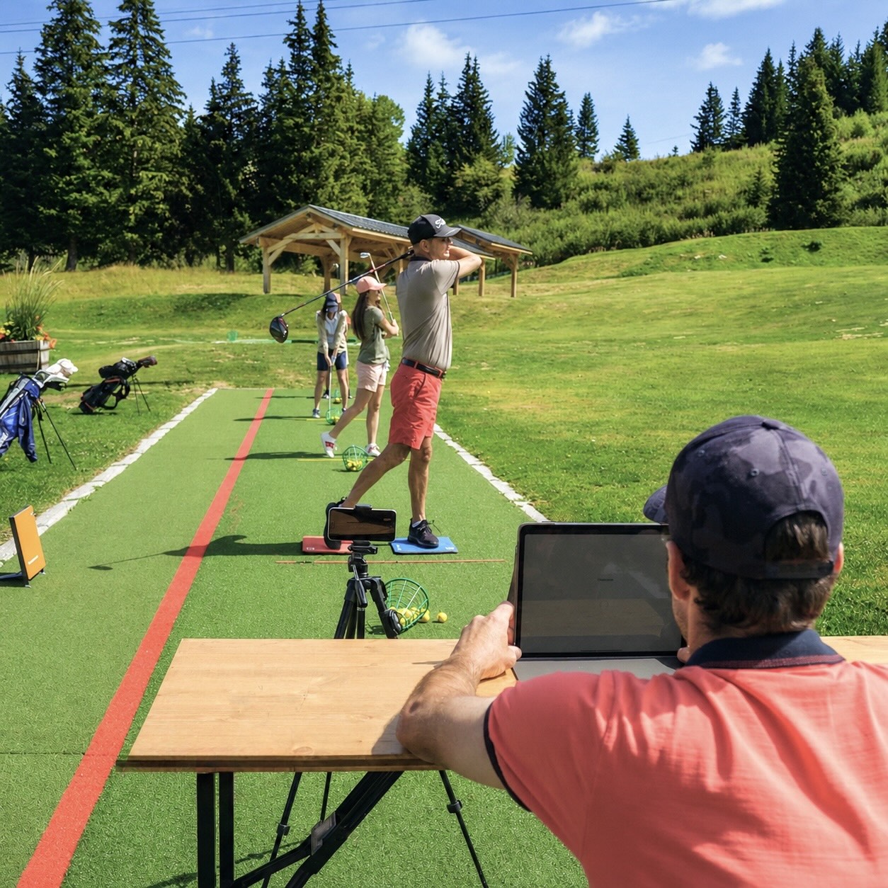 Enseignant PGA analysant le swing de deux golfeurs lors d’un cours duo sur le practice du Golf Club de Courchevel.