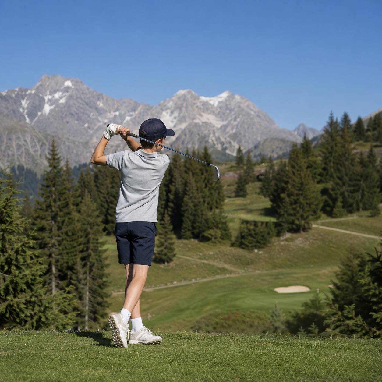 Young golfer playing a shot on the Courchevel Golf Club course with the Alpine mountains in the background.